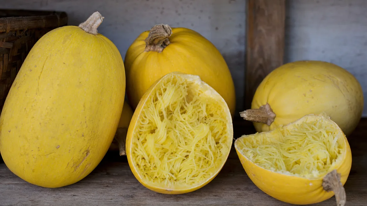 Whole golden yellow spaghetti squash and two cut halves showing pale strands on a rustic wooden shelf